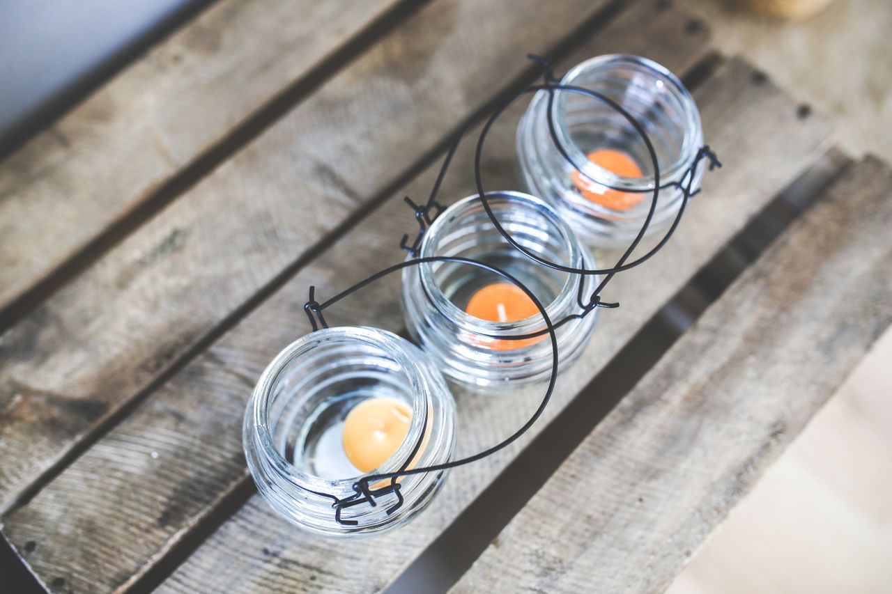 services-01 Top view of glass candleholders with orange tealights on a wooden surface.