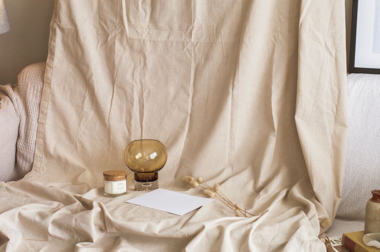 A cozy minimalist setup with beige fabric, a candle, and a glass vase for calming home decor inspiration.