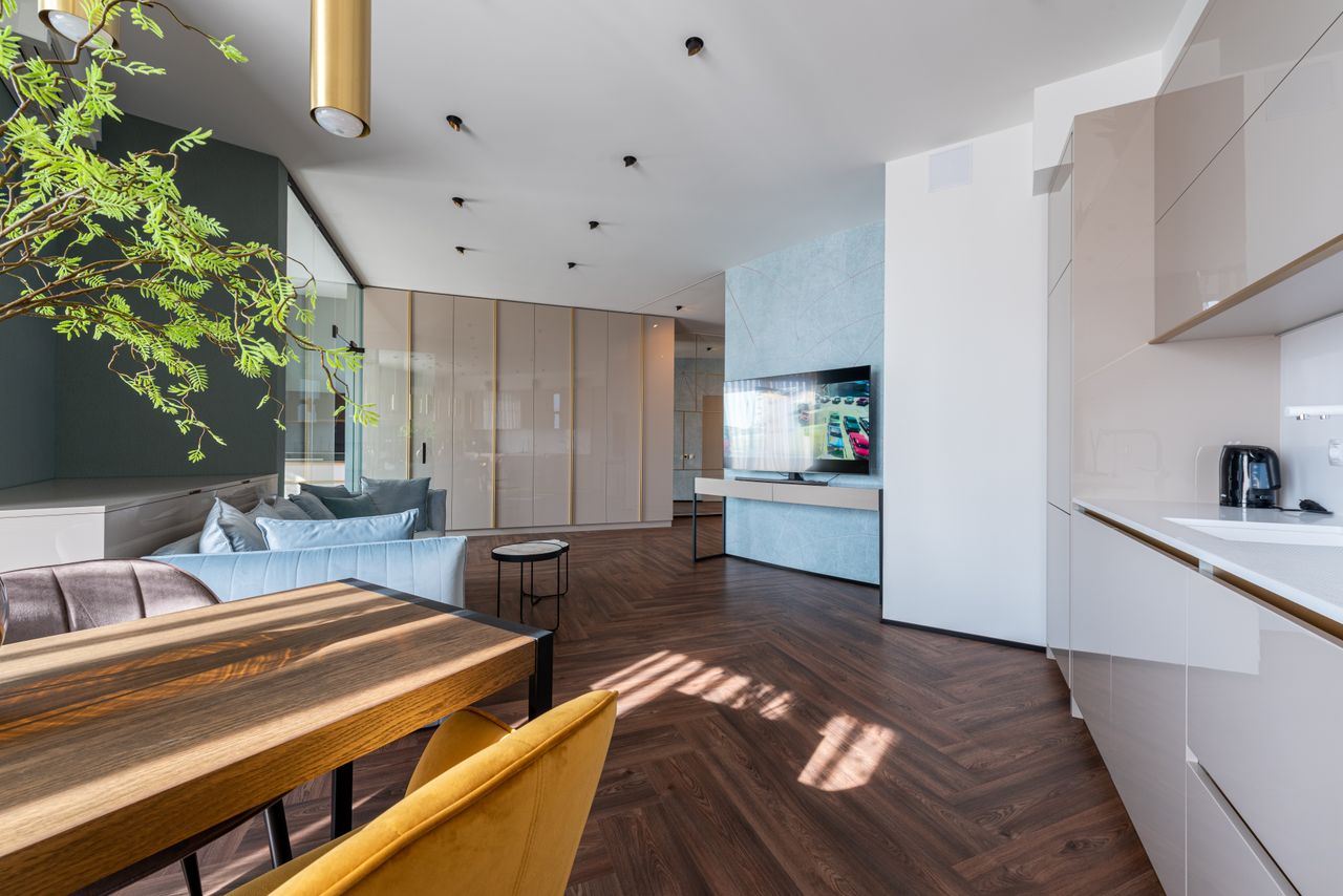 Kitchen interior with cabinets and wooden table placed near couch against wardrobe and TV set in modern apartment at home