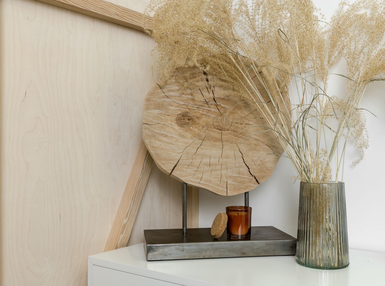 A stylish interior decor setting featuring dried plants in a glass vase and wooden accents.